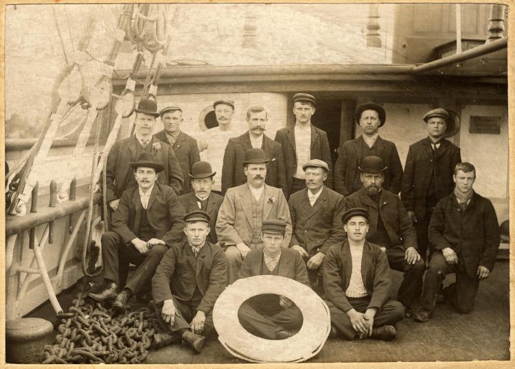 Three rows of men posed on a ship's deck.