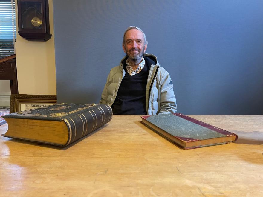 Man sits at table smiling with two large books on the table