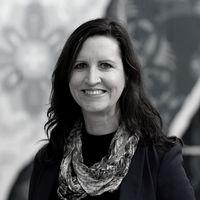 Black and white headshot of a women with dark hair wearing a black shirt and pattern scarf smiling facing the camera