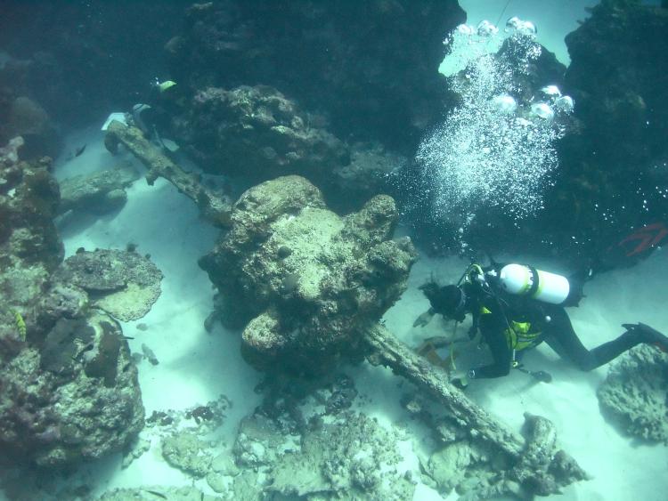 Two divers near a long thin piece of metal with a bulky protrusion in the middle.