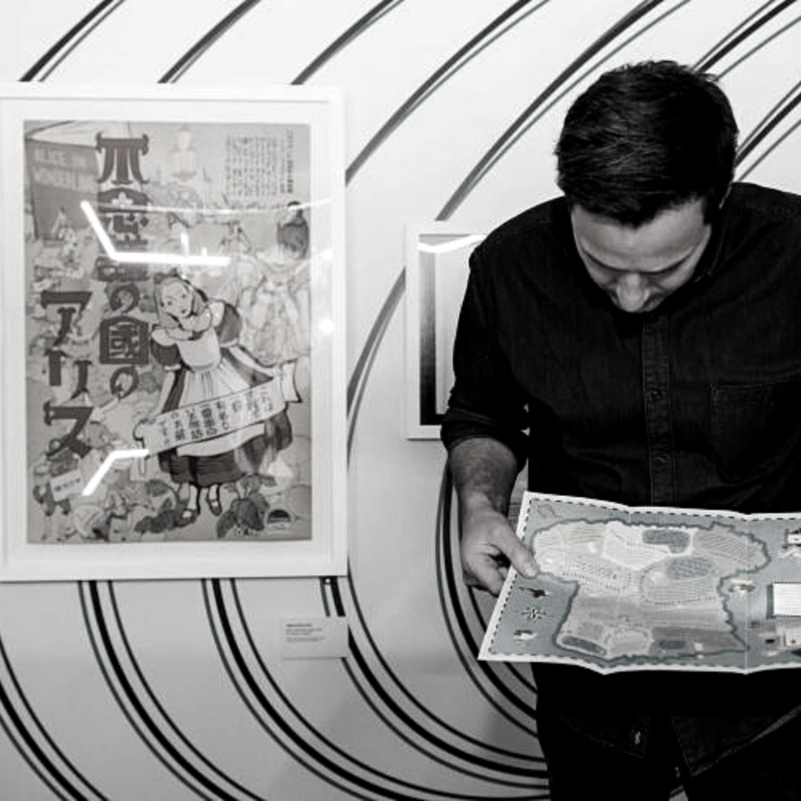 Black and white image of a man holding a map infront of a pattern print wall