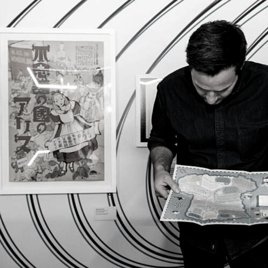 Black and white image of a man holding a map infront of a pattern print  wall