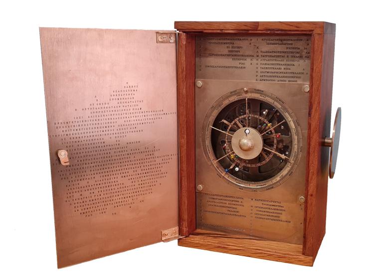 A brass model of the front of the Antikythera mechanism displaying a large dial with coloured hands, surronded by Greek symbols