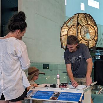 A volunteer wearing a WA Museum tee shirt demonstrates a model lighthouse to a small child