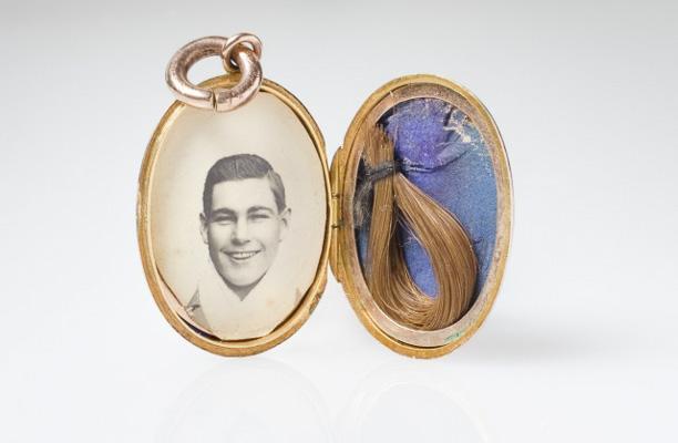 A small golden locket opened to reveal an old photograph of a smiling man on the left side, and a snipping of light brown hair on the right.
