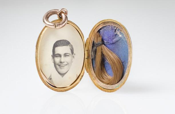 A small golden locket opened to reveal an old photograph of a smiling man on the left side, and a snipping of light brown hair on the right.