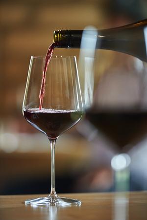 A large rectangular wine glass with a red wine being poured into it.