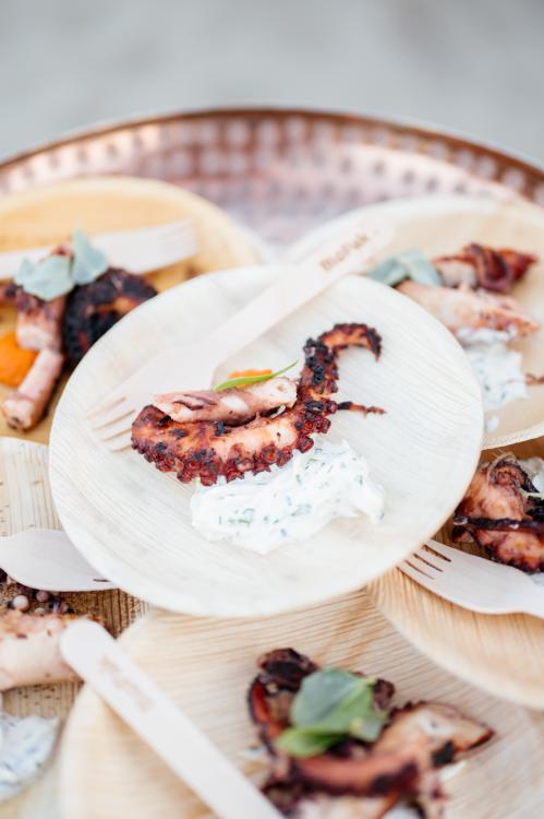 A piece of charred calamari with prosciutto and sauce on a bamboo plate