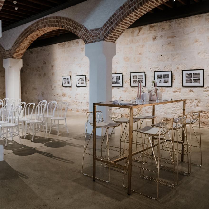 Chairs and tables are arranged for a wedding in a large room with limestone walls and an arched ceiling