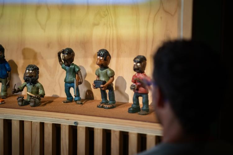 A person stares at a series of small figures made out of clay from the Bush Mechanics series, which all wear T-shirts and trousers can carry individual items like a car battery and hunting rifles