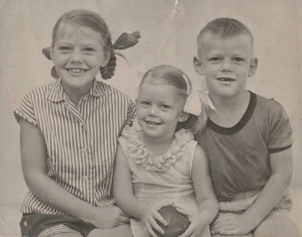 black and white photo of Sabrina Hahn as a child, Sabrina is around 6 years old and sitting in a posed photograph with her older siblings on either side 