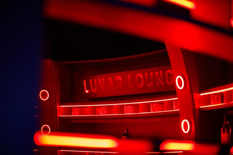 The words Lunar Lounge are etched into a sci-fi styled bar which is bathed in dramatic red light.