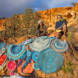 Two people sitting on a rock surrounded by a vibrant pile of colorful rugs.