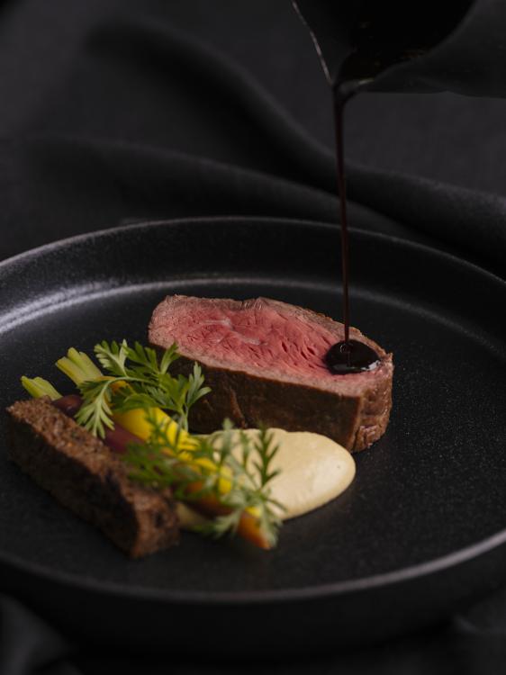A plate of food, mainly beef, on a dark plate