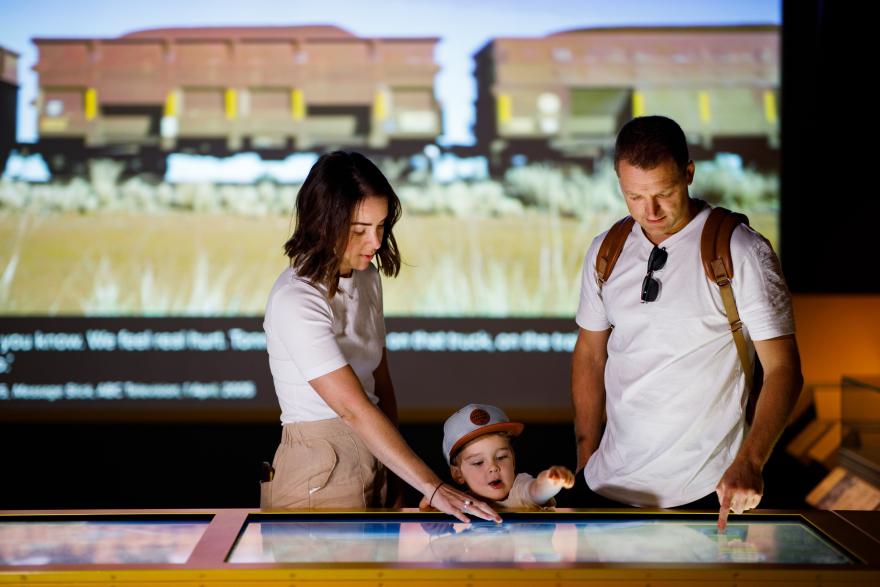 Family interacting with a touchscreen exhibit, with a train video projected in the background.
