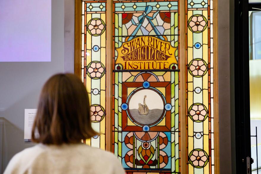 Person viewing a stained glass window with text and a swan image.