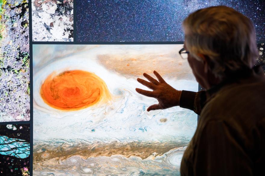 Person pointing at a display of Jupiter’s Great Red Spot amidst a collage of other geological and astronomical panels.