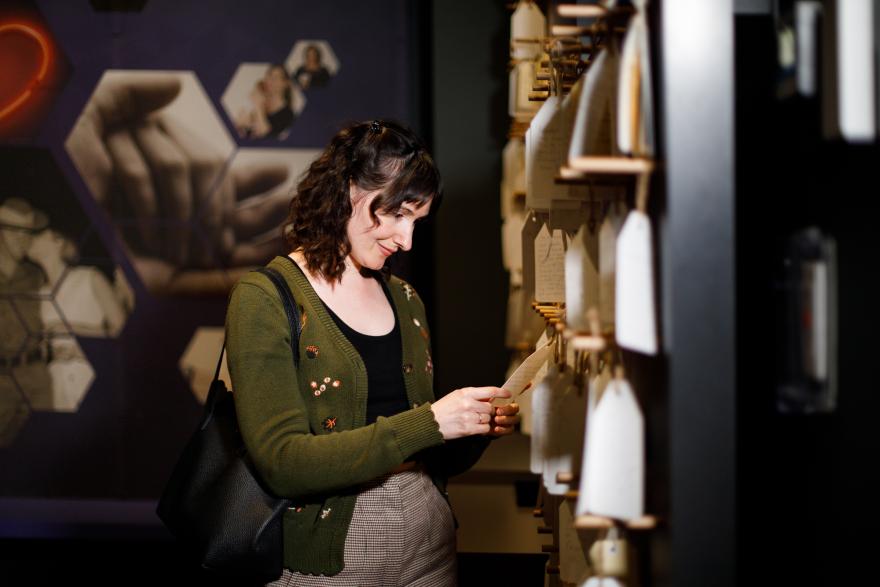 Woman reading a note from an installation of hanging tags in an exhibition space.