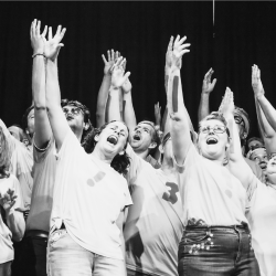  A vintage black and white photo of a group of people with their hands raised in the air.