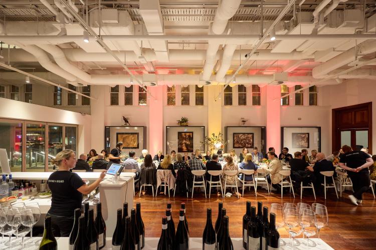 Indoor dining event with a long communal table, people dining, and a bar in the foreground.