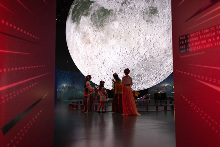 A group of people standing in front of a large display moon in a Museum gallery