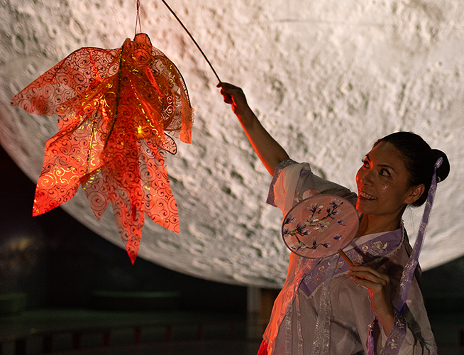 A person standing in front of a large moon display in traditional dress