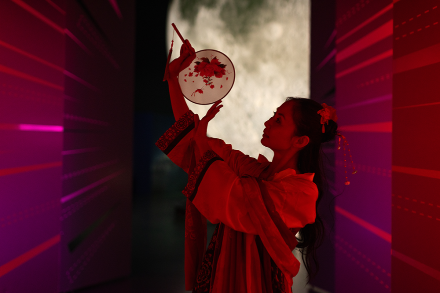 A person holding up a beautiful fan in front of a large display moon