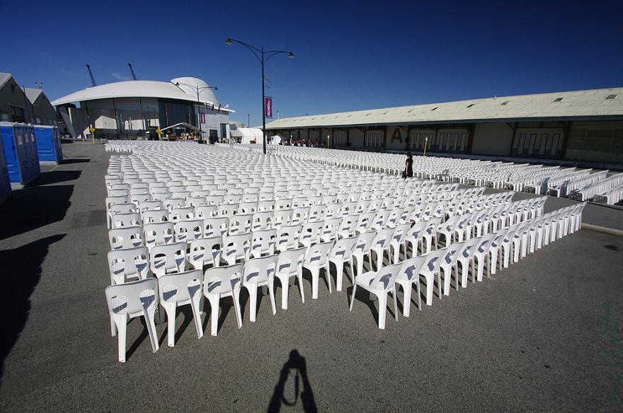 Rows of white plastic chairs on pavement with the dome-shaped roof of the Maritime Museum in the background.