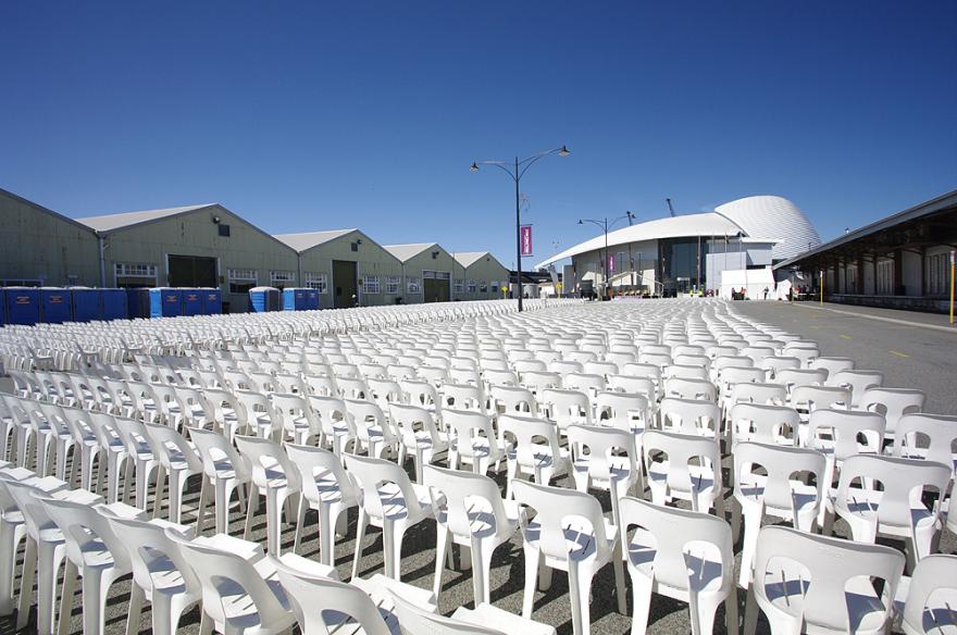 Rows of white plastic chairs on pavement with the dome-shaped roof of the Maritime Museum in the background.