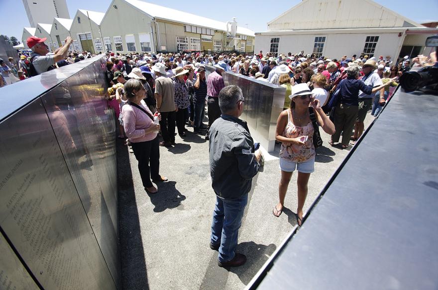 Crowd gathered in an outdoor quay examining metal panels with engravings of names.