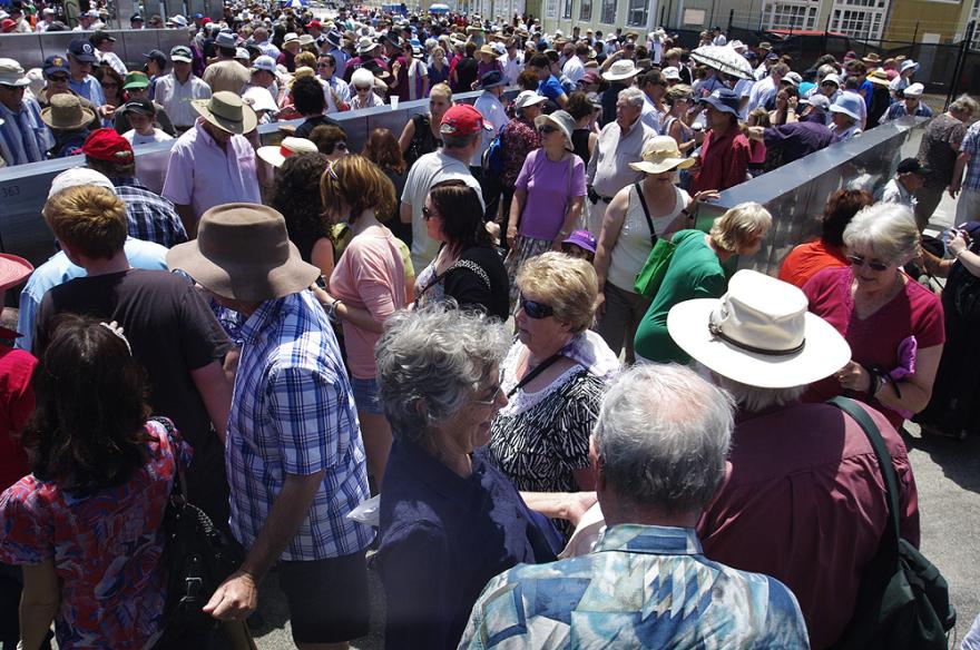A large crowd gathered in an outdoor quay examining metal panels with engravings of names.