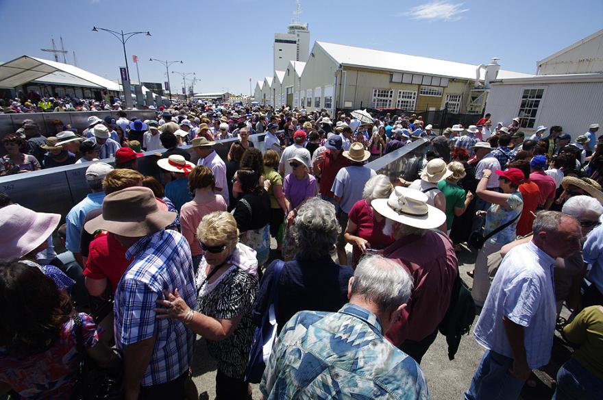 A large crowd gathered in an outdoor quay examining metal panels with engravings of names.