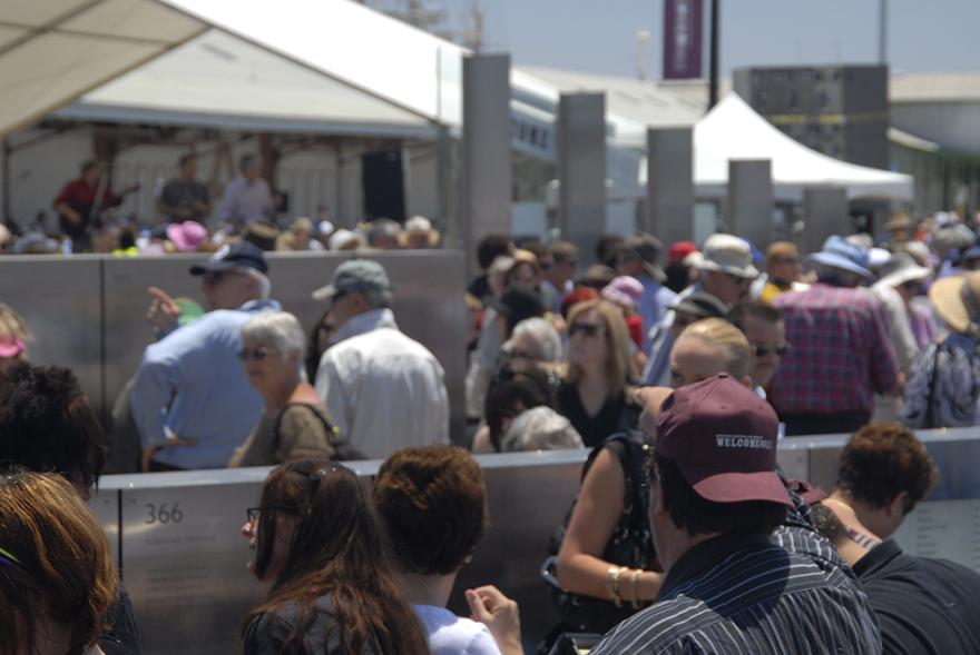 A large crowd gathered in an outdoor quay examining metal panels with engravings of names.