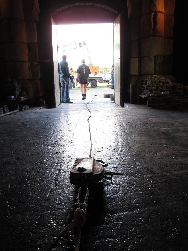 Dark room with a rope leading to a bright open doorway where silhouettes of two people are visible.