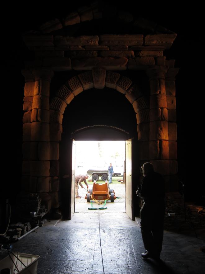 Dark room leading to a bright open doorway where an individual attends to a large cannon.