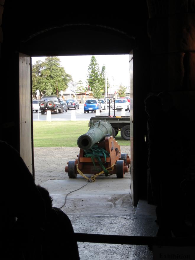 Dark room leading to a bright open doorway where a large cannon is tethered to a rope system.