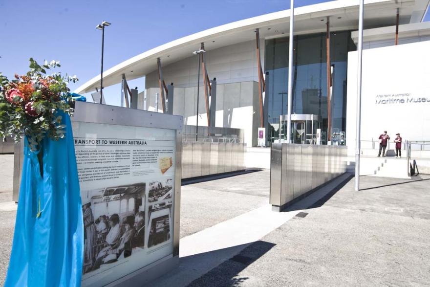 Entrance of the Western Australia Maritime Museum with an informational display on Transport to Western Australia, and floral arrangement in the foreground.