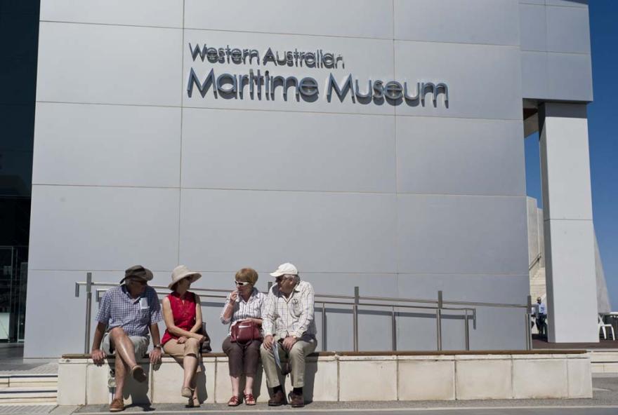 Four people sit on a stone bench outside of the white Western Australian Maritime Museum building