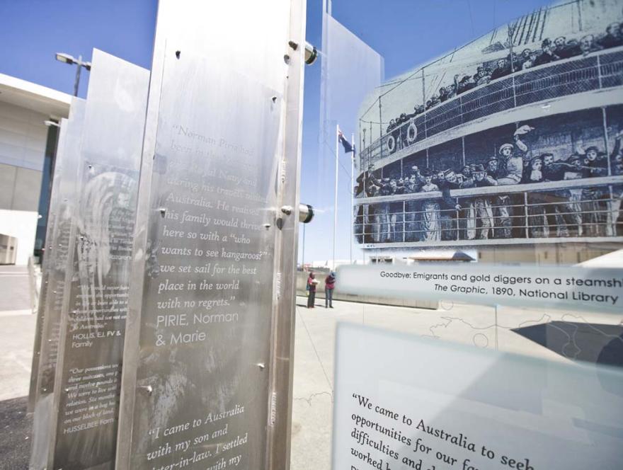 Several rows of engraved metal and glass panels with quotations and information and an illustration of people standing at a ship's barriers