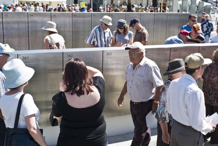 A crowd of people examining engraved metal walls with names and dates on a sunny day