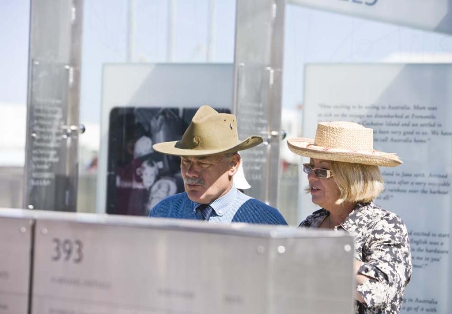 Two individuals wearing hats read from an engraved metal wall with great interest
