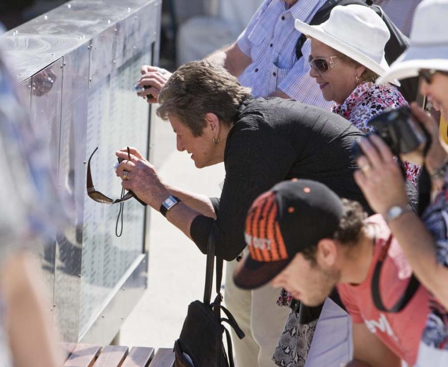 A crowd of people reading names off of an engraved glass panel