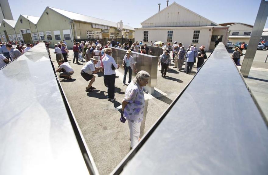 A crowd of people examining engraved names on rows of metal panels on a sunny day