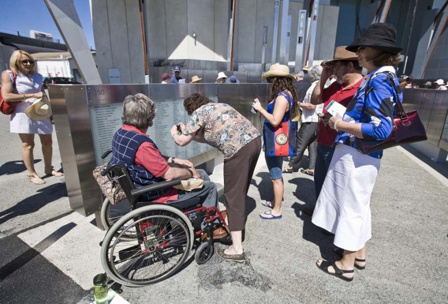 A crowd of people reading names off of an engraved glass panel and taking photographs