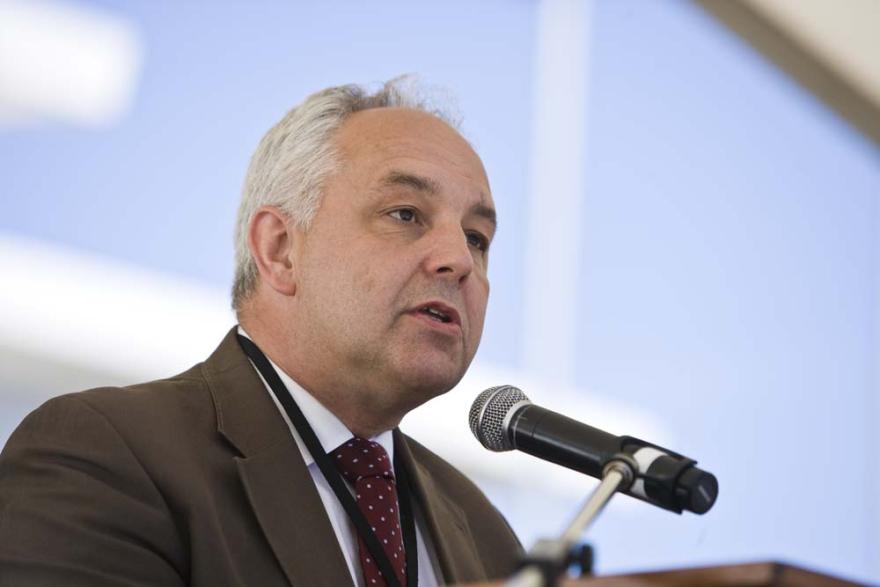 A close up on a person wearing a brown suit and red tie and speaking into a microphone