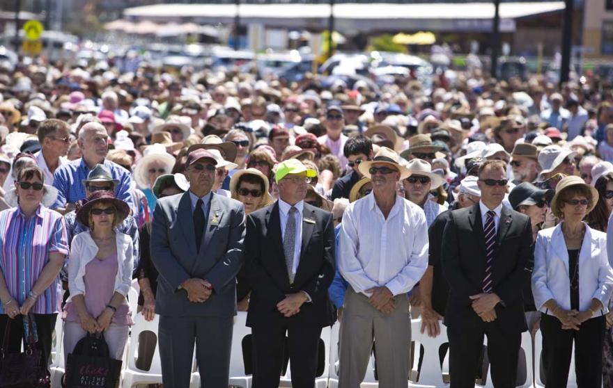 Rows of individuals stand with the hands crossed in front of them, with the rows stretching back across a large space.