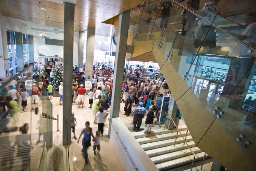 An internal of a white modern building with a large staircase to the right. A large crowd fills the space.