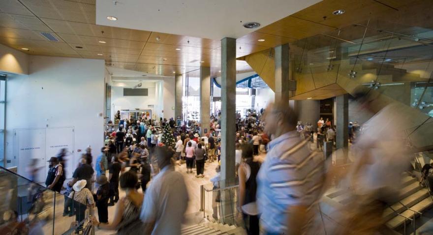 An internal of a white modern building with a large staircase to the right. A large crowd fills the space.