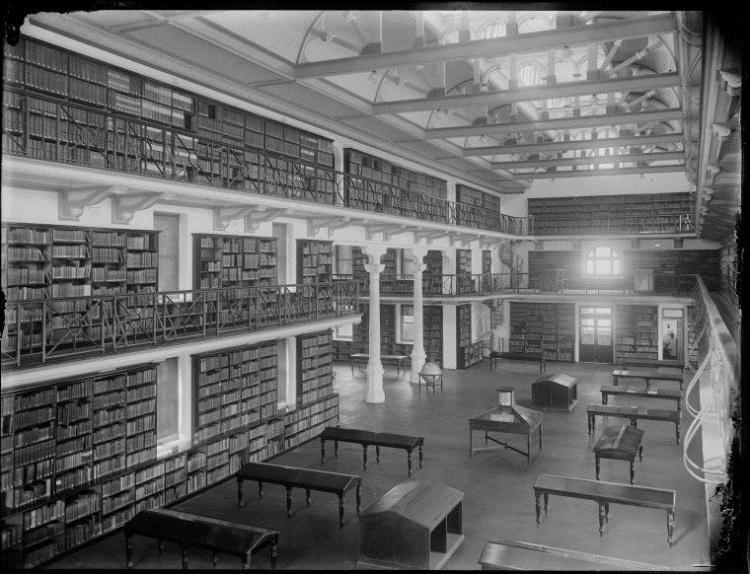 Historic library interior with bookshelves, balcony, and tables.