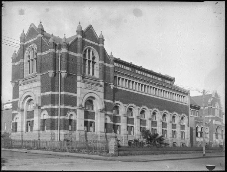 A black and white image of a large Gothic-style brick building with arched windows and decorative stonework.